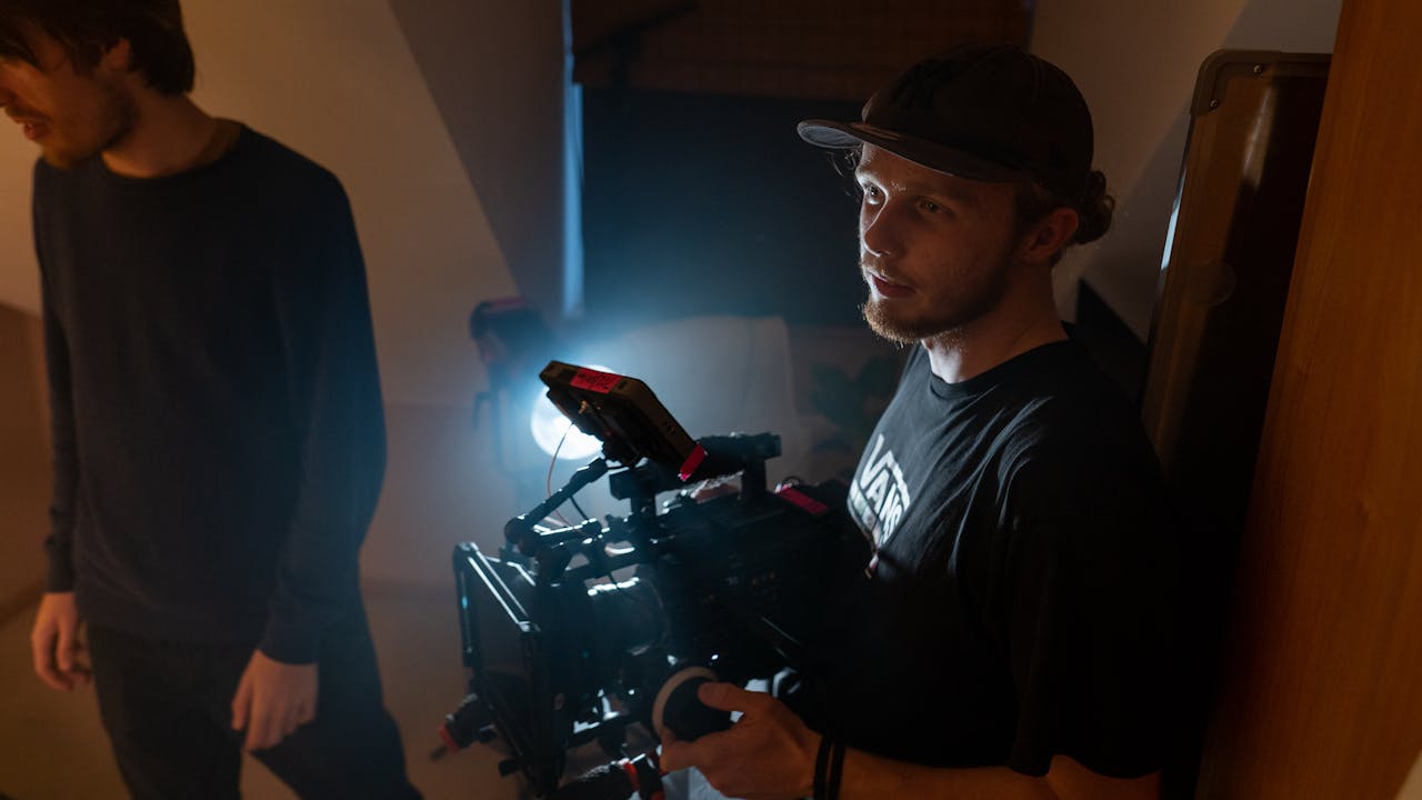 A filmmaker focuses intently while operating a camera on an indoor film set.