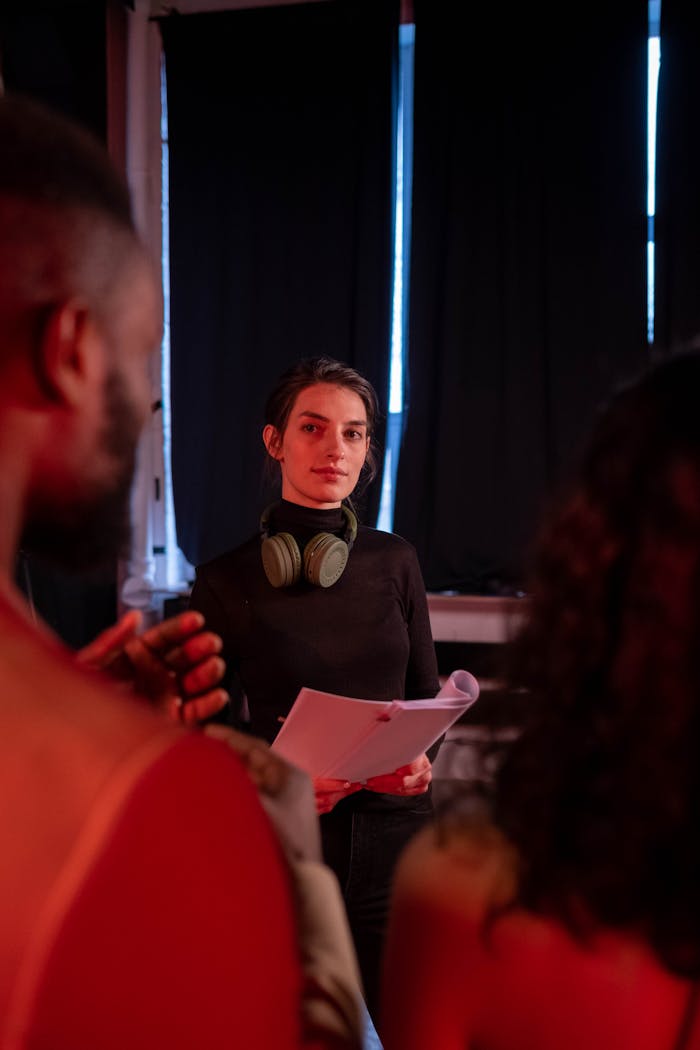 A female director holding script and wearing headphones on a film set indoors.